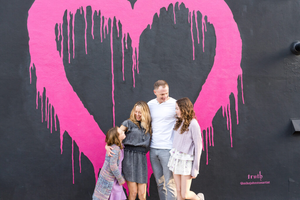 A bright pink heart painted on a black wall on the streets of Austin serves as the backdrop for the end of this family's photo session with Alissa Cordoba.