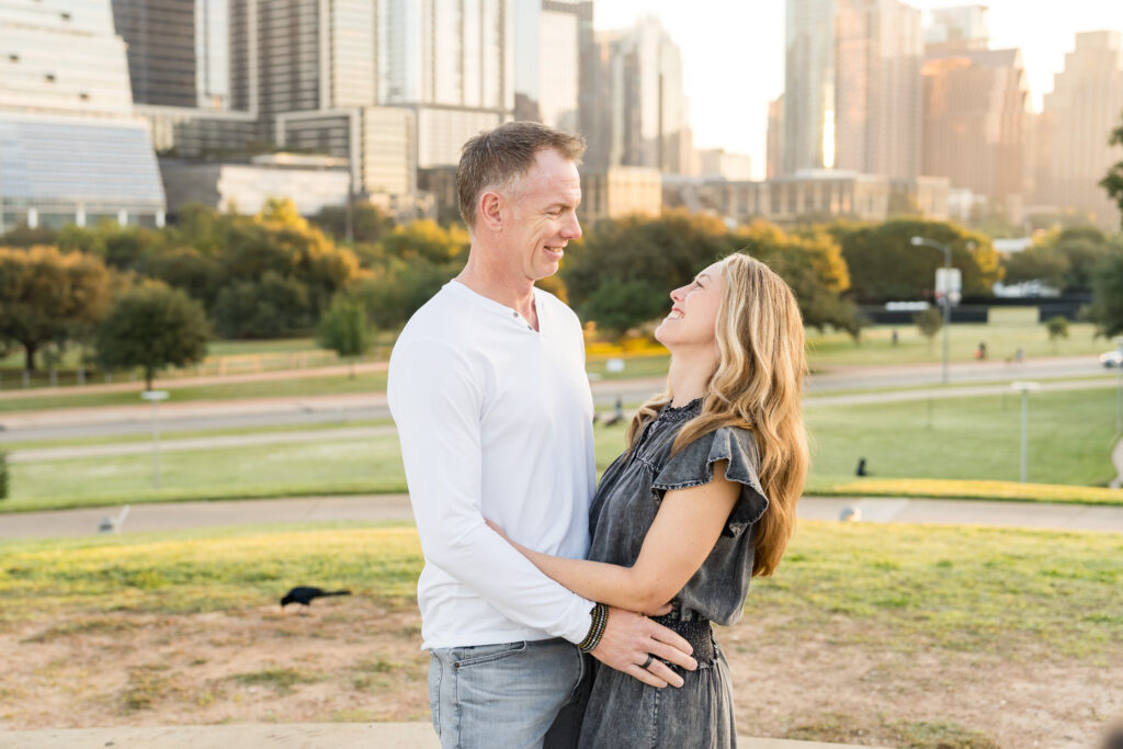 A husband and wife holding onto one another at the waist and smiling as they look at each other.