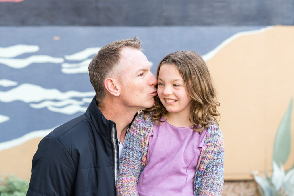 A father giving a quick kiss on the cheek to his daughter.