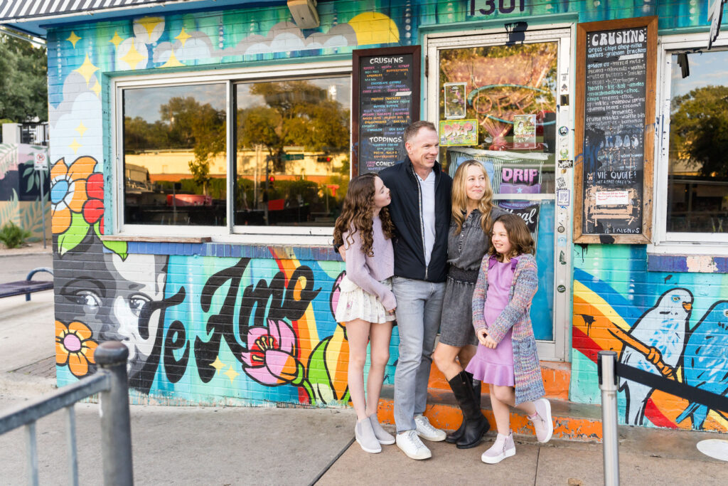 A family posing for a photo during their family session in Austin, Texas, in front of a colorful cafe.