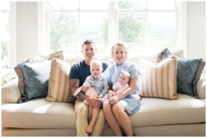 A family sitting on the couch in front of their large bay window as they have their first family portraits taken with their newborn.