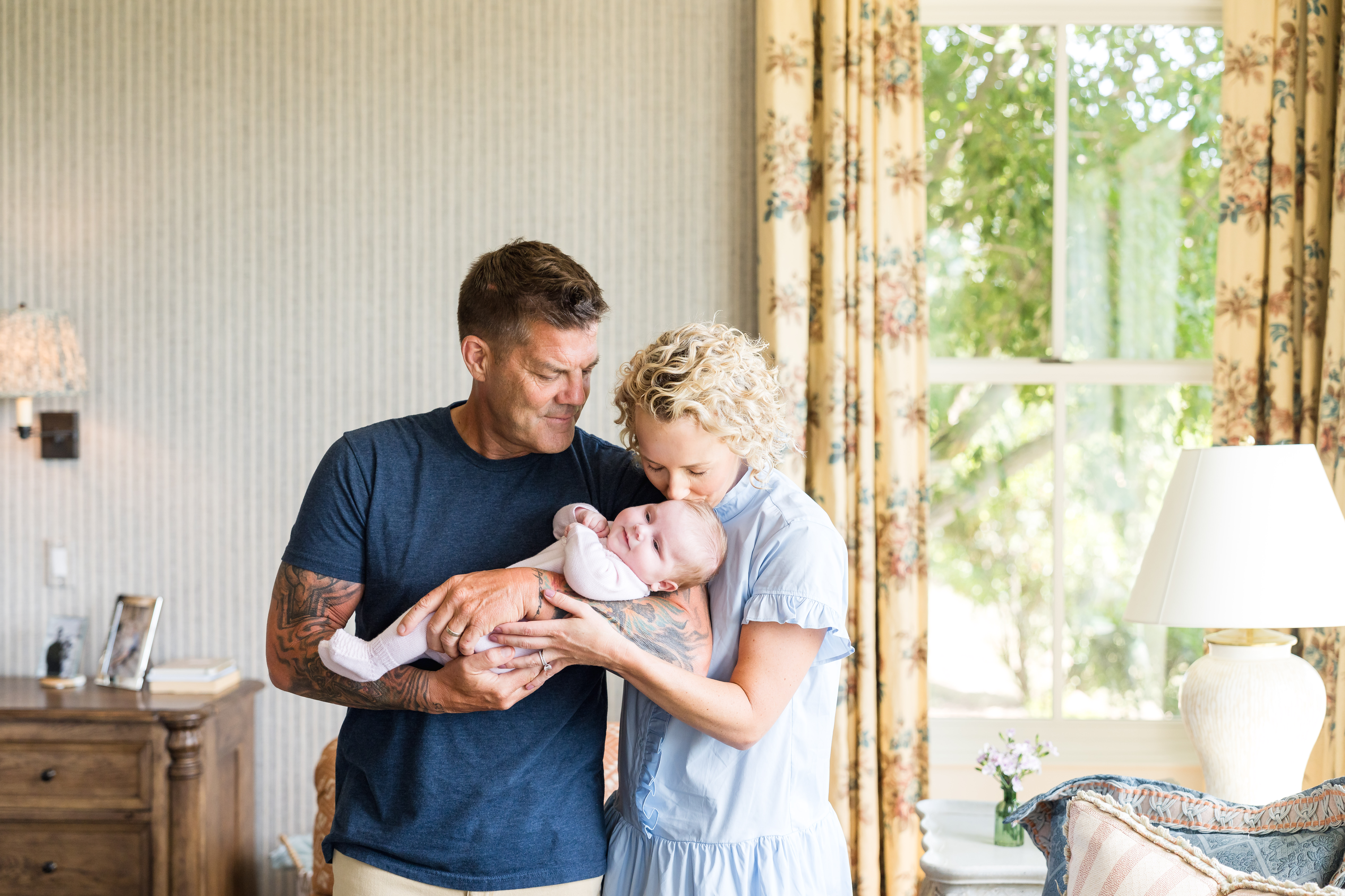 A new dad holding his daughter as mom kisses her forehead during their newborn photography session at their home in Austin.