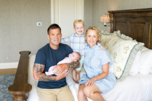 A family gathered together in the master bedroom of their home in Austin as they hold their daughter during newborn photography session with Alissa Cordoba Photography