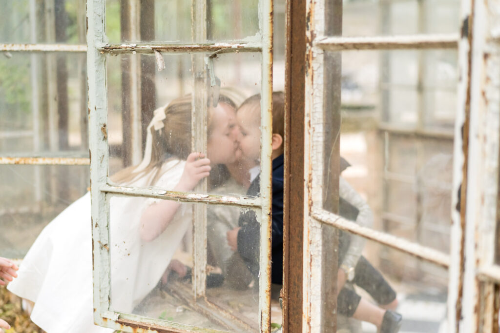 A brother and sister giving each other a kiss through a window in the greenhouse at Sekrit Theater.