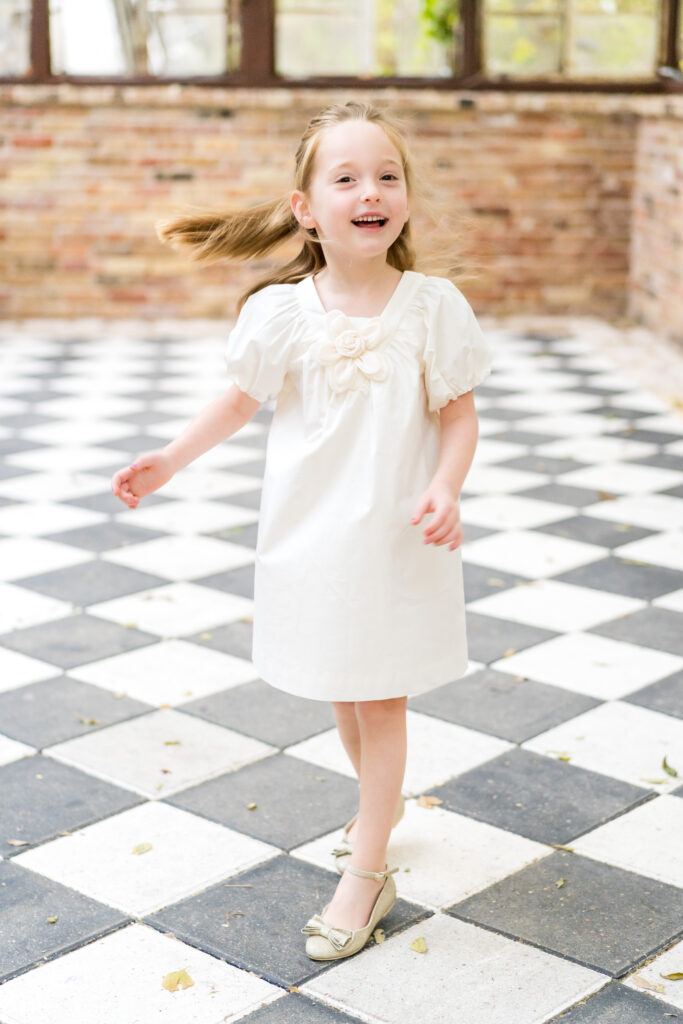 A young girl twirling in a cream dress at the greenhouse located at Sekrit Theater in Austin.