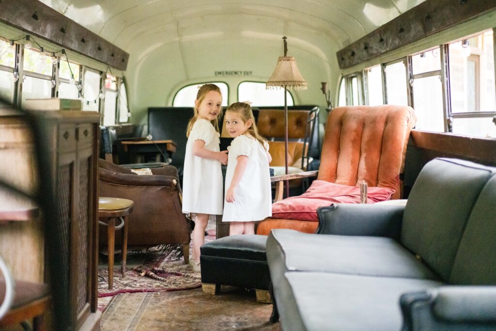 Two young sisters looking over their shoulder at the camera as they play on the bus that is located at Sekrit Theater, one of Austin's best family photography locations.