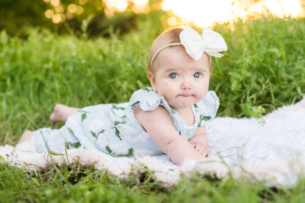 A 6 month old girl laying on a blanket in the grass during her photo session.
