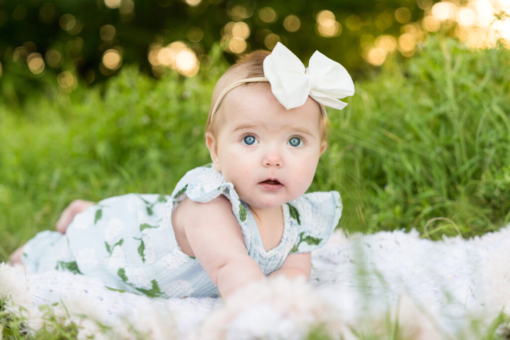 A 6 month old girl laying on a blanket in the grass during her photo session.