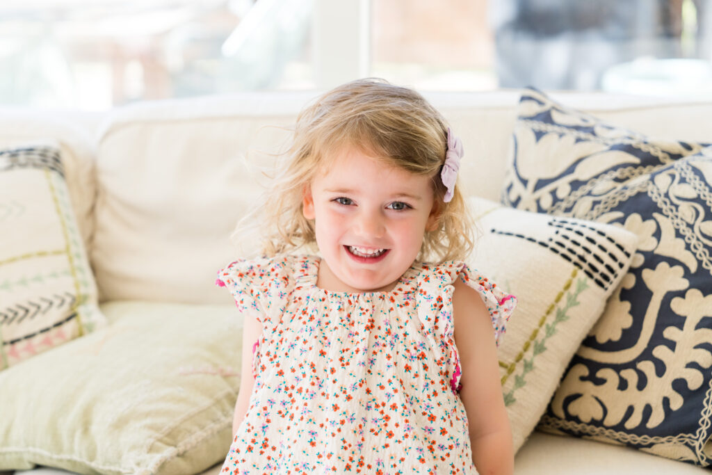 A big sister smiling, wearing a dress with small flowers, while having her photo taken.
