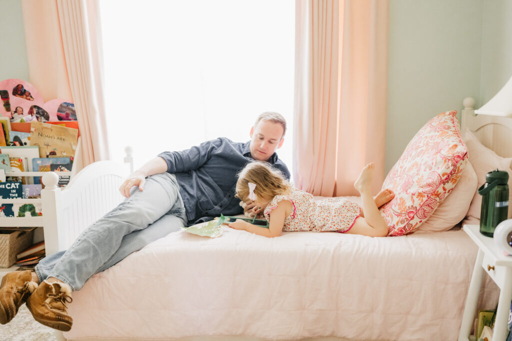 A father and daughter reading a book on her bed during their in-home lifestyle session.