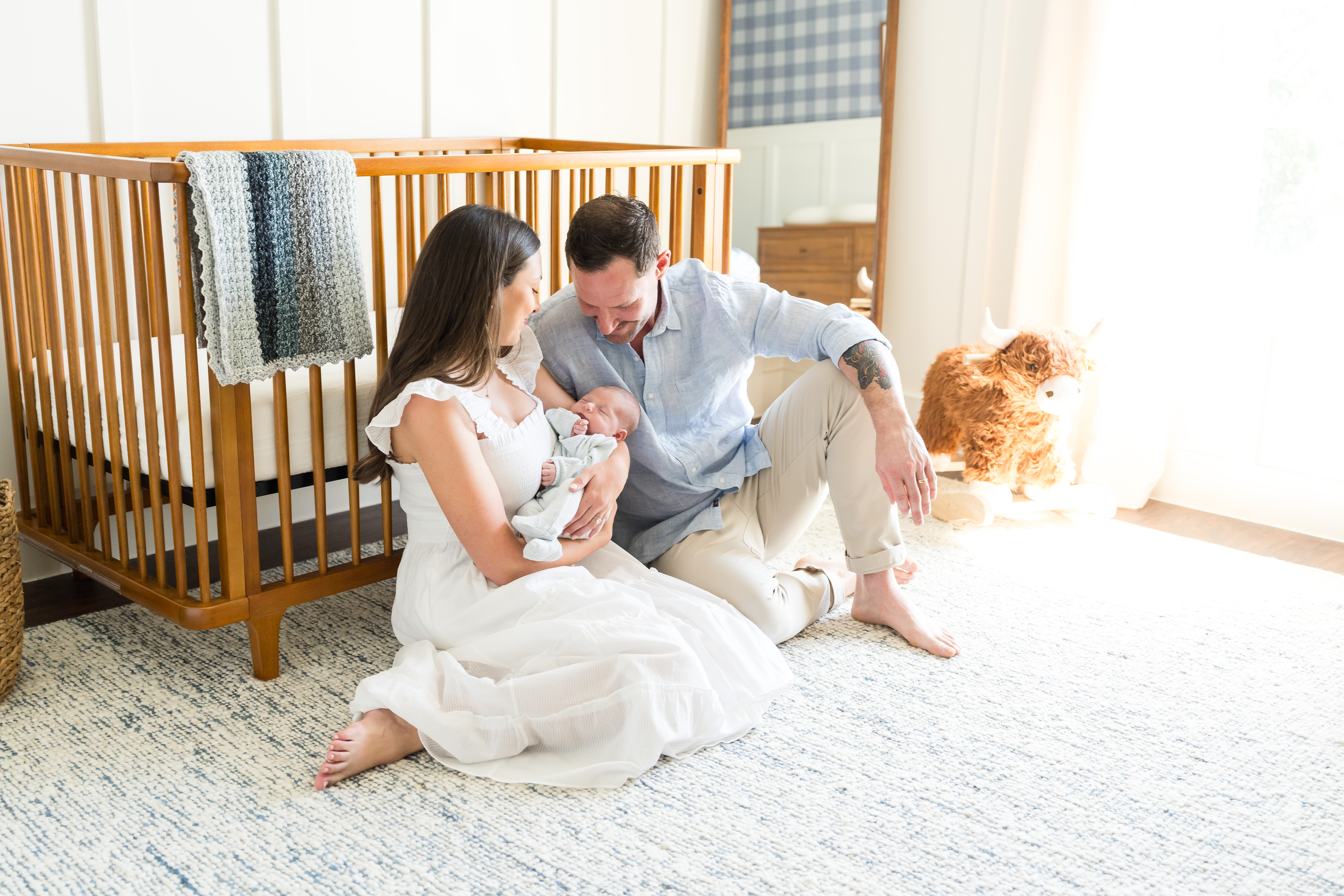 Mom and dad sitting in the nursery with their newborn during their lifestyle newborn photo session.