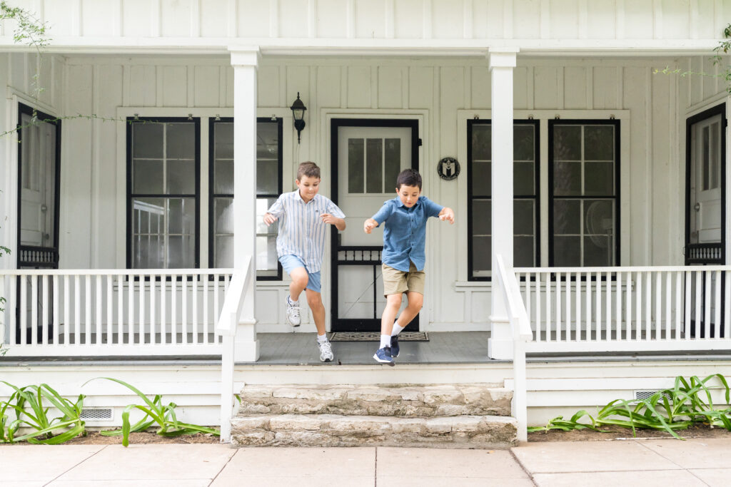 Two brothers jumping off the front porch of a house in Austin during their family photo session.